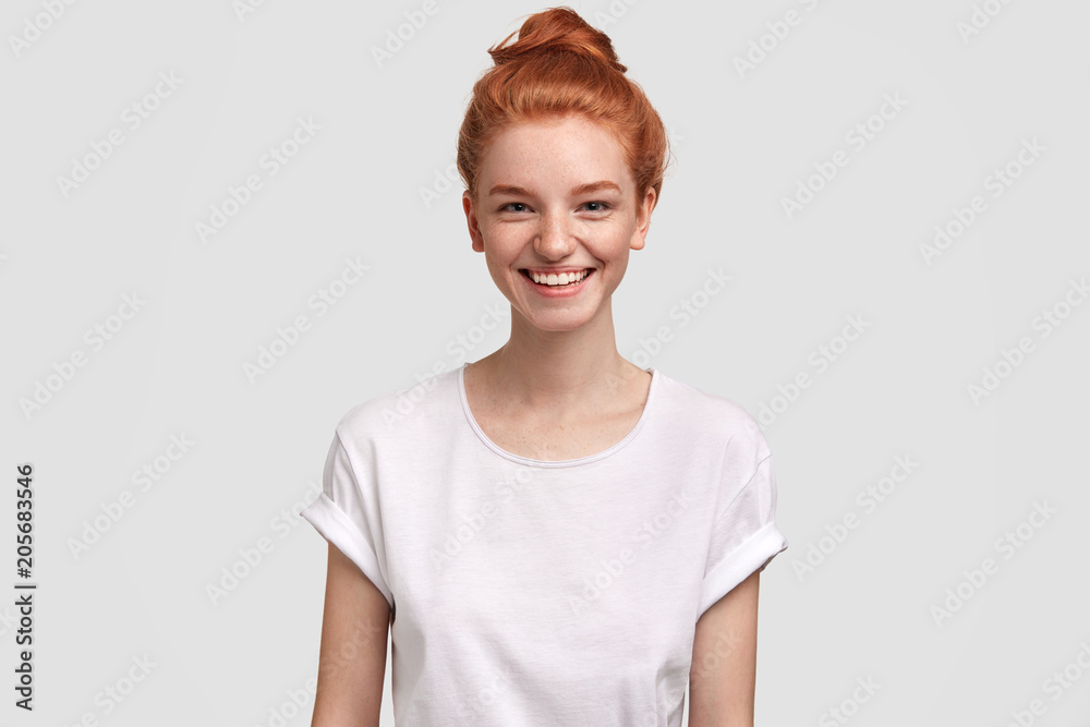 Waist up portrait of delighted freckled redhead woman with pleasant smile, wears casual white t shirt, rejoices good news, isolated over studio background. Foxy female teenager spends time with friend Waist up portrait of delighted freckled redhead woman with pleasant smile, wears casual white t shirt, rejoices good news, isolated over studio background. Foxy female teenager spends time with friend