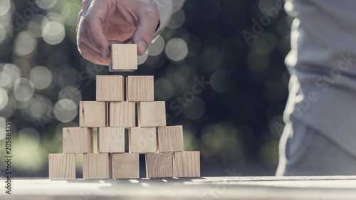 Retro toned image of man building a pyramid with blank wooden blocks outdoors photo