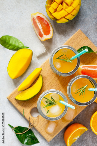 Fresh refreshing summer drinks. Multifruit drinks of citrus and mango with ice, smoothies on a light stone or slate background. Copy space, top view flat lay background.