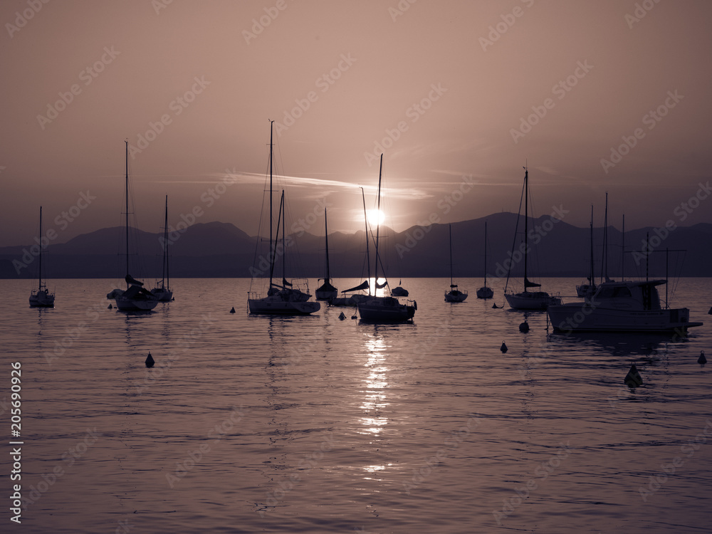 Sailboats moored in Lake Garda, Italy, at sunset.