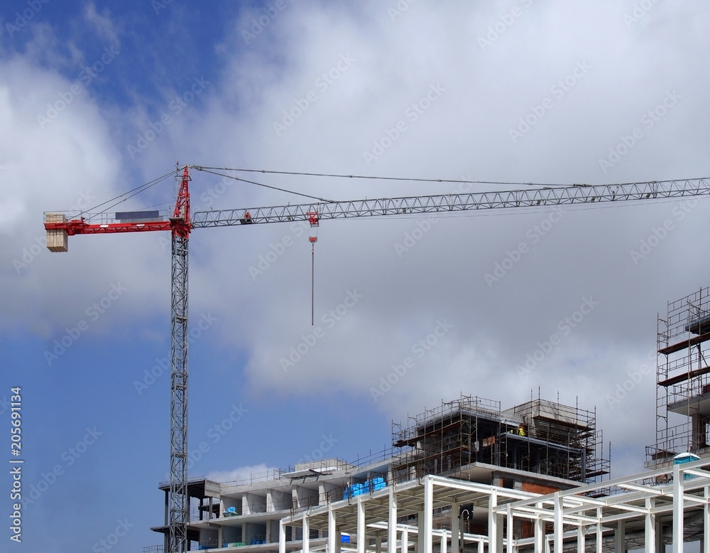 tall red crane on a large construction site with metal framework scaffolding blue sky and clouds
