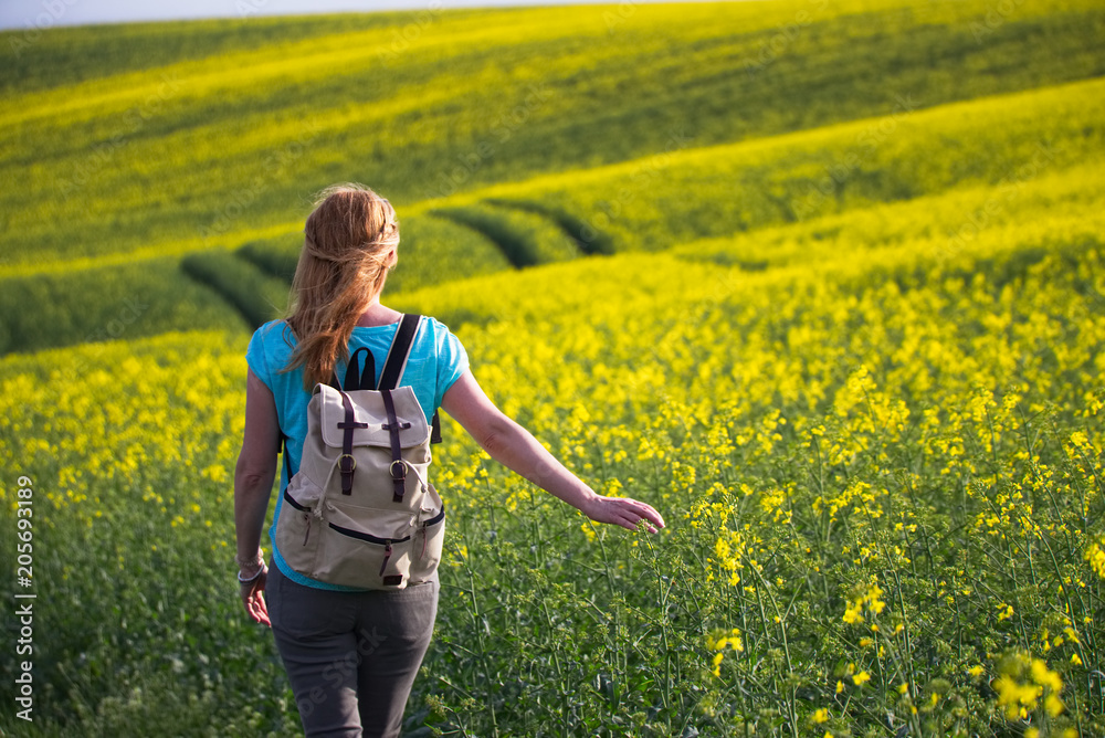 Happy woman with backpack in blooming oilseed field