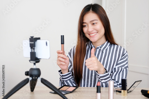 Young asian woman beauty blogger showing how to makeup video tutorial while recording by smartphone