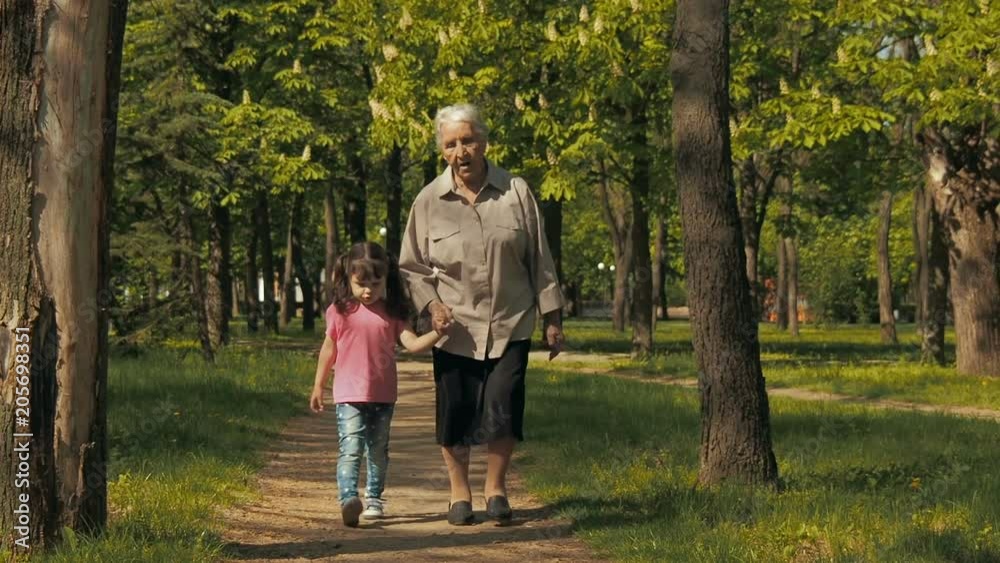An elderly woman with a child is walking in the park. Grandmother with granddaughter on a walk in the park. An elderly woman with a child is walking in the park. Grandmother with granddaughter on a walk in the park.