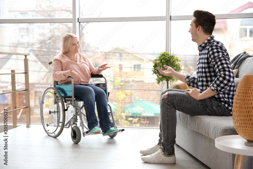 Young man talking to mature woman in wheelchair indoors Young man talking to mature woman in wheelchair indoors