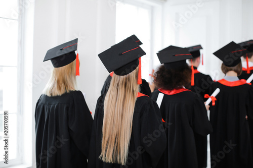 Students in bachelor robes and mortarboards indoors. Graduation day