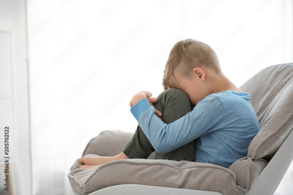Lonely little boy sitting on chair at home. Autism concept