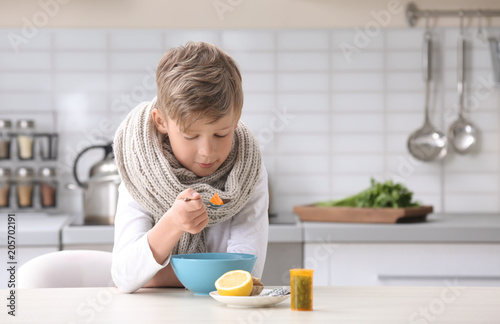 Sick little boy eating broth to cure cold at table in kitchen