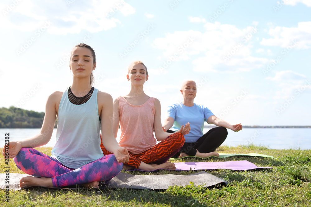 Group of women practicing yoga near river on sunny day Group of women practicing yoga near river on sunny day