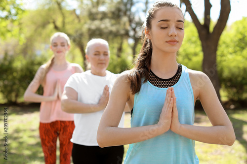 Group of women practicing yoga in park on sunny day