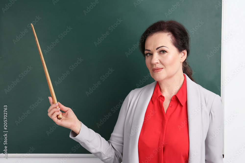 Portrait of female teacher with pointer near chalkboard in classroom Portrait of female teacher with pointer near chalkboard in classroom