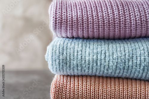 Stack of warm knitted clothes on grey background
