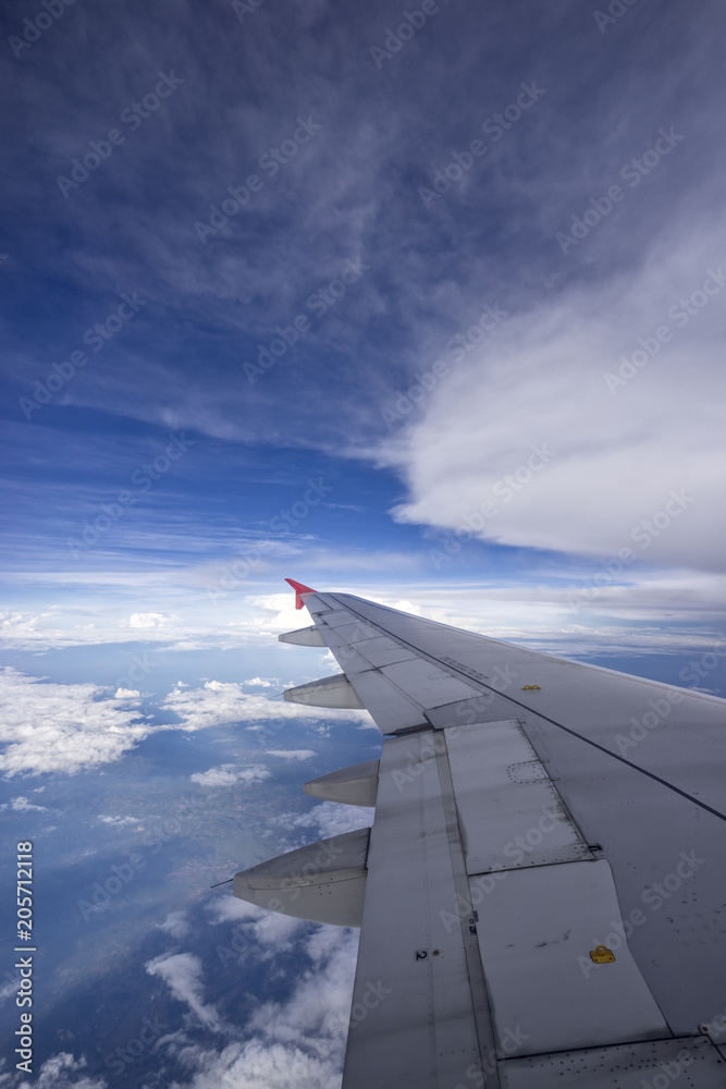 Beautiful clouds with blue sky, through airplane window, aircraft wing on a side.