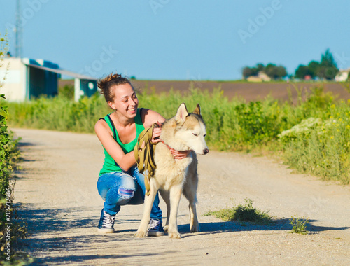 Happy young woman smiles and strokes a hussy dog among the fields. Paddling of pets.