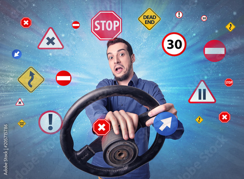 Young man holding black steering wheel with road signs surrounding him