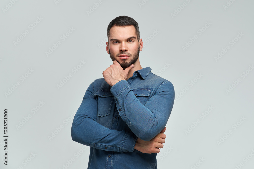 attractive young confident man with interest and in thought folded his hands on chest and holds his hand to chin and beard. attractive young confident man with interest and in thought folded his hands on chest and holds his hand to chin and beard.