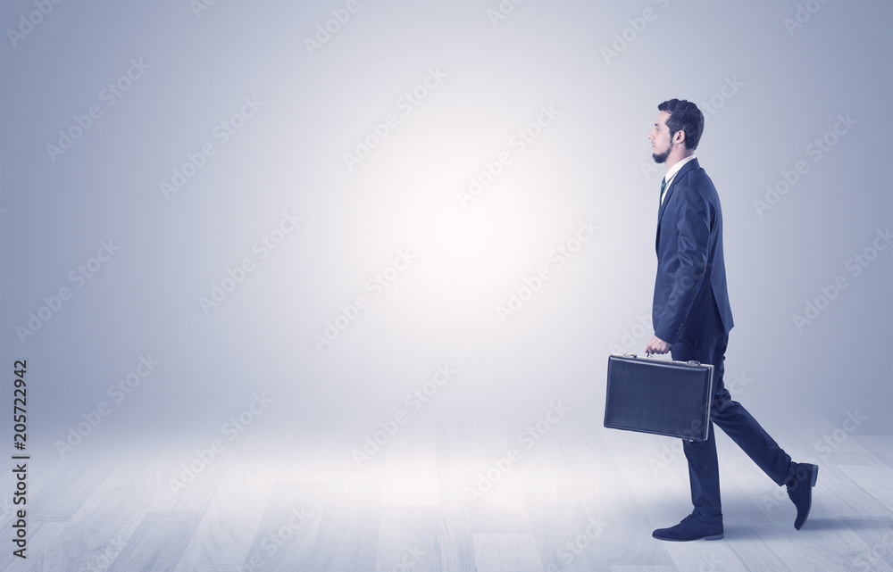 Successful businessman walking in front of an empty wall with briefcase on his hand
Successful businessman walking in front of an empty wall with briefcase on his hand