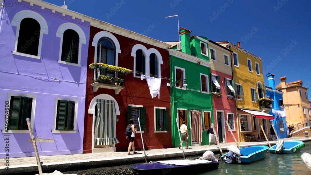 Curious tourists walking street on Burano island, photographing colored houses