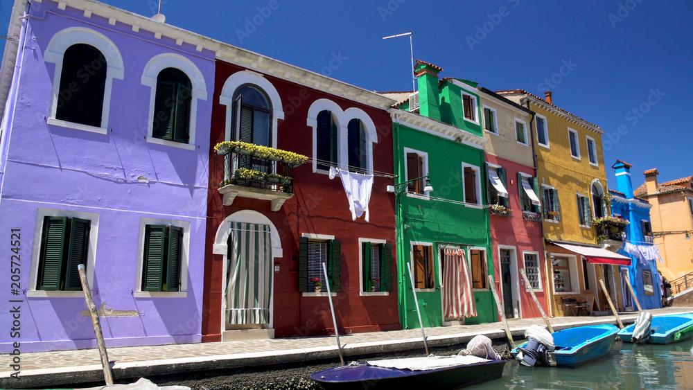 Brightly colored houses and boats at mooring points along canal on Burano island
