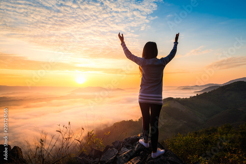 Young woman standing on top of the mountain watching the sun rise with fog