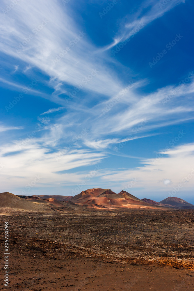 Volcanic crater in the Timanfaya National Park under a blue sky with clouds. Lanzarote, Canary Islands, Spain. Volcanic crater in the Timanfaya National Park under a blue sky with clouds. Lanzarote, Canary Islands, Spain.