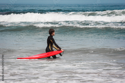 Young boy with a red surf waiting for a wave. Famara beach, Lanzarote, Canary Islands, Spain. © Giulio