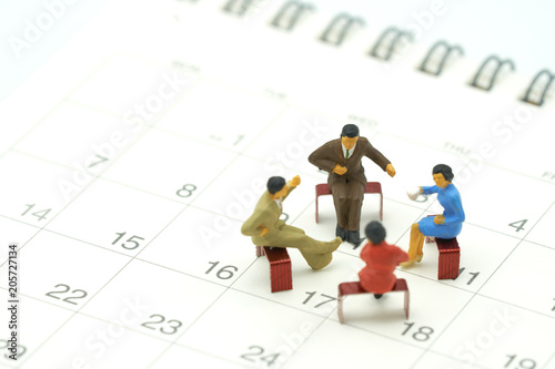 Miniature 4 people sitting on red staples placed on a white Calendar. meeting or Discussion using as background business concept with copy space and white space for your text or  design.
