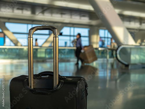 Black carry on luggage sitting at modern airport with workers in background