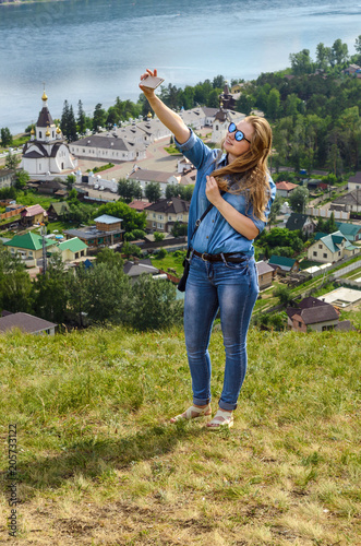 Fototapeta Naklejka Na Ścianę i Meble -  A young girl in blue clothes makes selfie on the background of a beautiful landscape