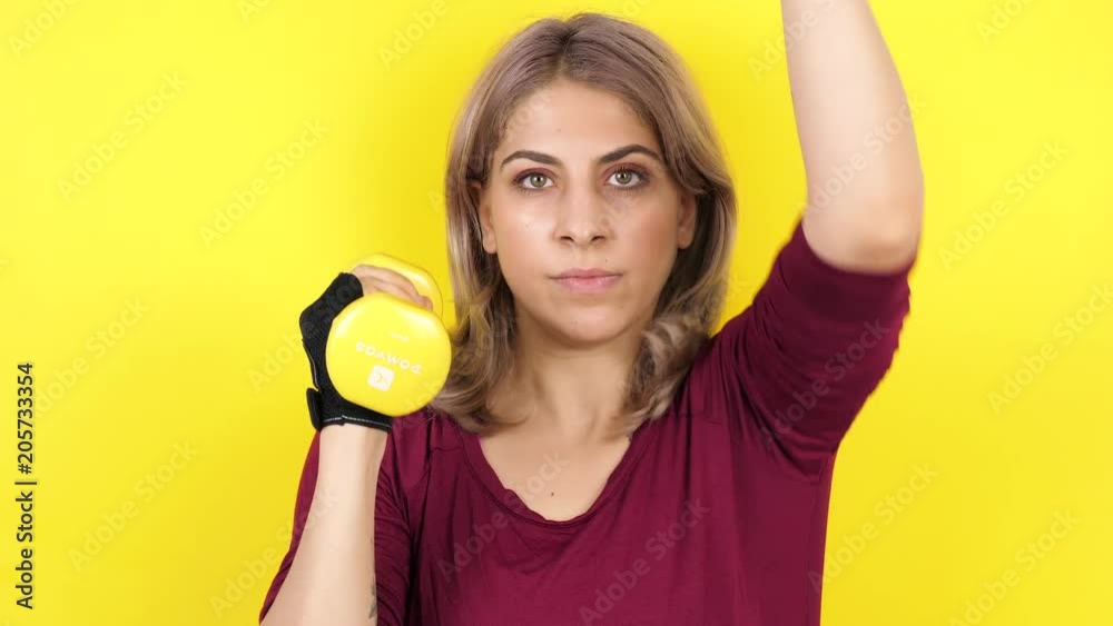 Woman practicing sport with dumbbells on yellow background in studio Woman practicing sport with dumbbells on yellow background in studio