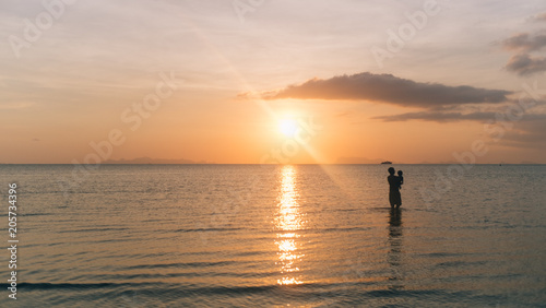 Silhouette Dad and son are walking together on the beach and sea with the sunset background and copy space.