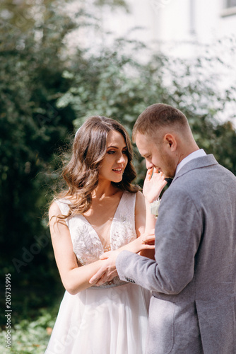 Portrait of a beautiful couple in love on your wedding day. Walking near the house with white walls and greenery. Amazing kisses and embraces of the bride and groom with a bouquet