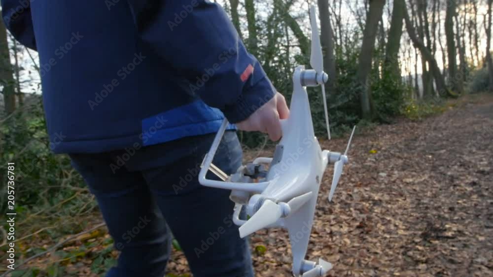 A person in a blue jacket goes with a drone through the forest in slowmotion A person in a blue jacket goes with a drone through the forest in slowmotion