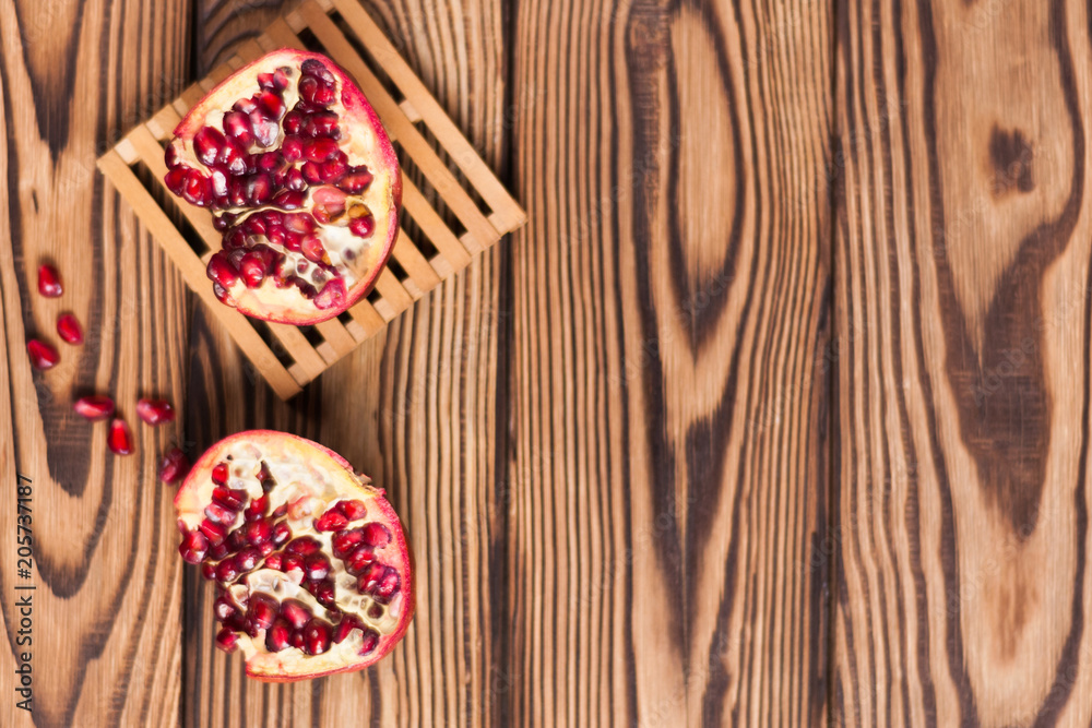 One half of red fresh ripe pomegranate with seeds on pallet beside one piece of pomegranate and scattered seeds on old brown weathered wooden planks. Top view One half of red fresh ripe pomegranate with seeds on pallet beside one piece of pomegranate and scattered seeds on old brown weathered wooden planks. Top view