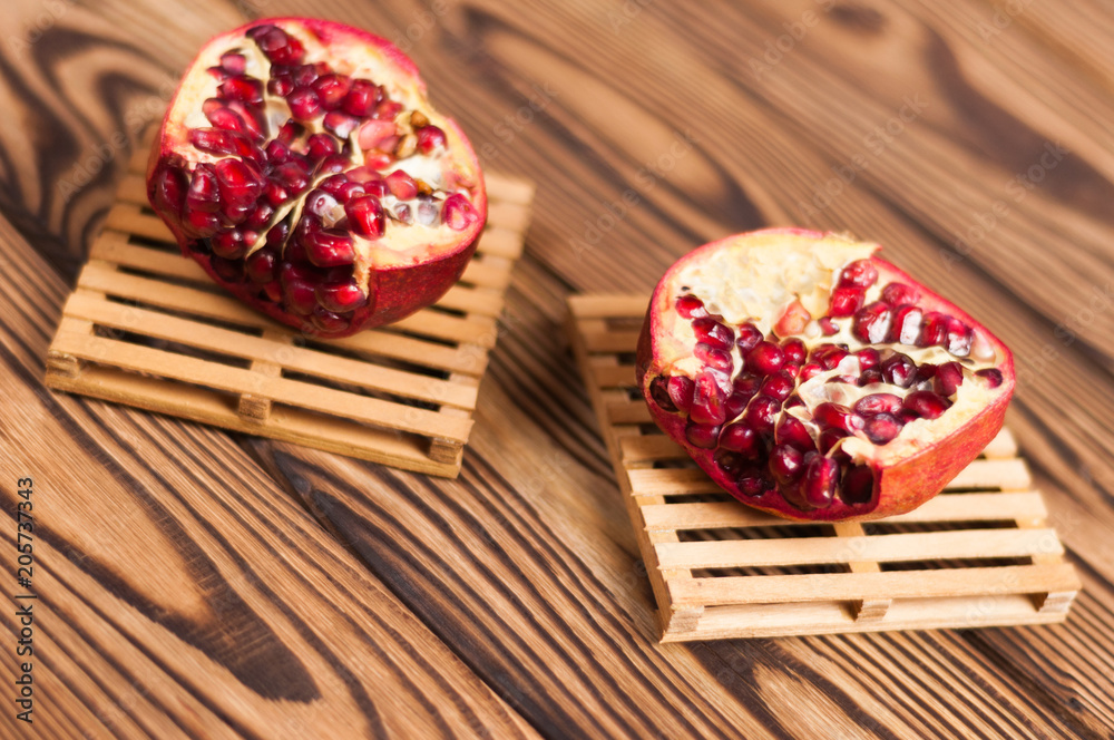 Two halves of red ripe fresh pomegranate on wooden pallets near scattered seeds on old brown weathered rustic planks Two halves of red ripe fresh pomegranate on wooden pallets near scattered seeds on old brown weathered rustic planks