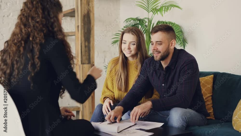 Young man is talking to housing agent, signing document and taking house key, clasping hands with realtor then kissing his wife. Buying real estate and people concept.