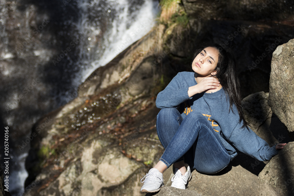 Mujer joven morena con pelo largo y liso sentada delante de una cascada Mujer joven morena con pelo largo y liso sentada delante de una cascada