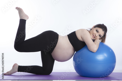 Pregnant woman is doing exercises with gymnastic ball on white background