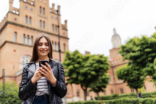 Single student walking and reading mobile phone messages with a university building in the background photo