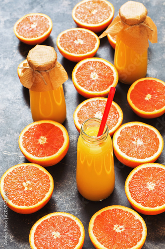 Orange juice in a bottle and halves of orange on a dark background.