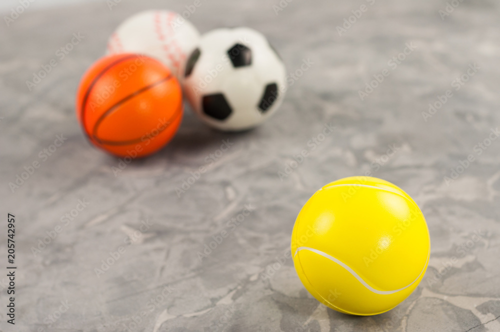 One new rubber soft tennis ball on background of three different sports balls on old worn cement