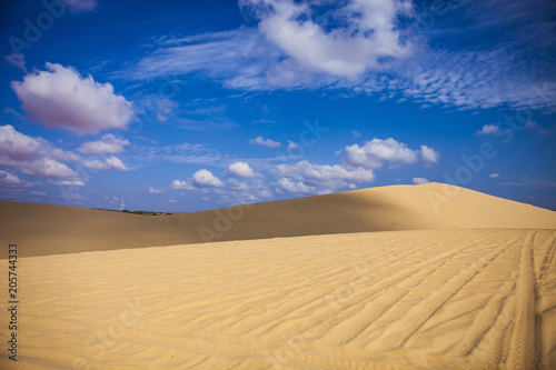Sand dunes near Mui Ne. Group of off roads on top of dunes in the background. Sunny day with blue sky and clouds