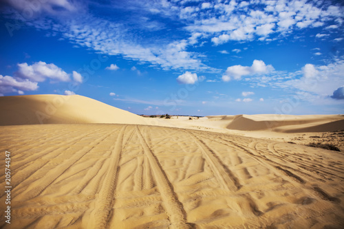 Sand dunes near Mui Ne. Group of off roads on top of dunes in the background. Sunny day with blue sky and clouds