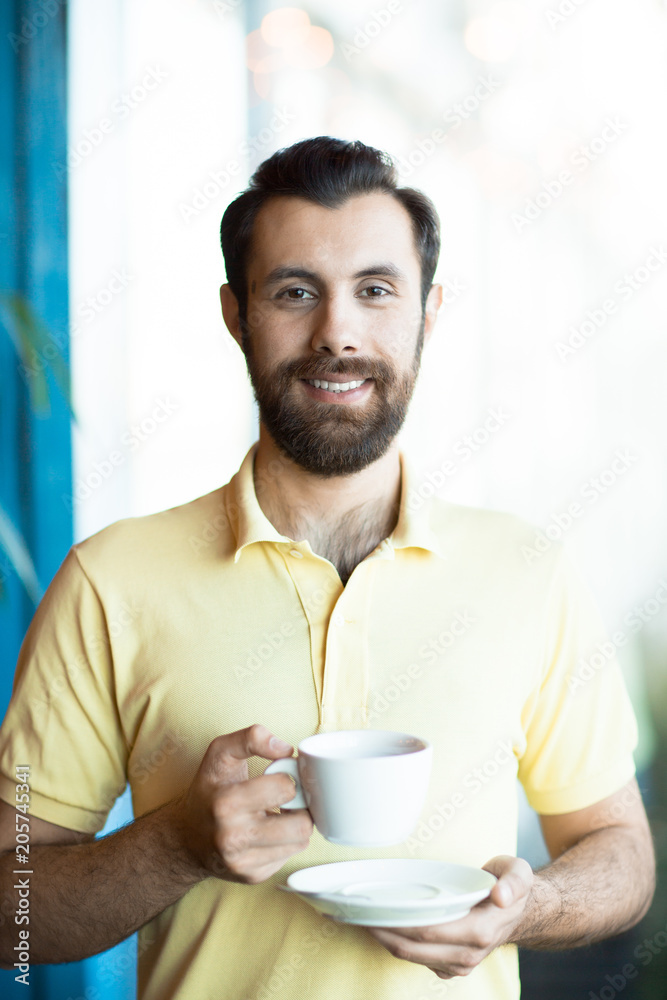 Young manager with cup of coffee looking at you with smile on one of working days Young manager with cup of coffee looking at you with smile on one of working days