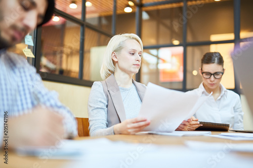 Serious young manager or accountant working with papers in office among her colleagues