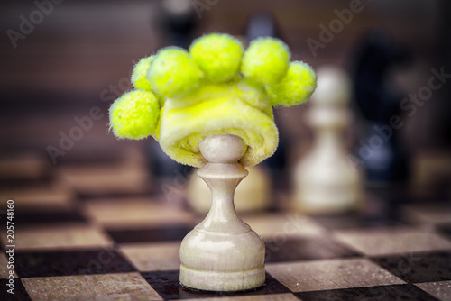 chess pawn in foolish hat in the center of the chess board - business failure concept if works alone without team and opposes itself to the collective. photo