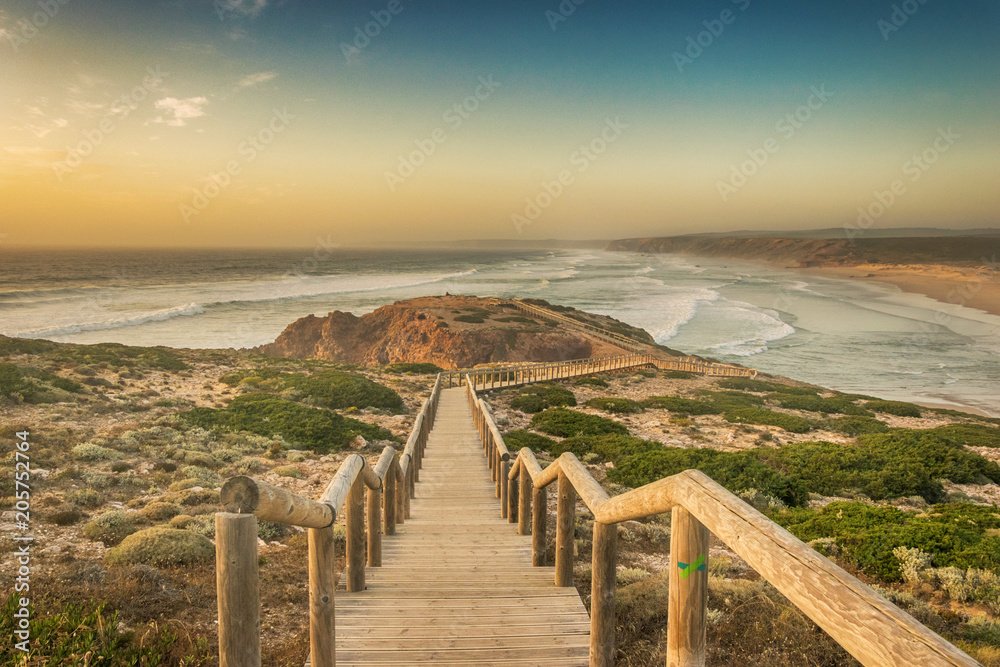 Wooden footbridge leading to the edge of a cliff above the ocean during sunset