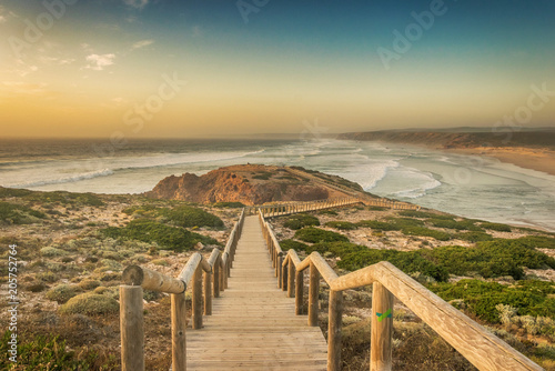 Fotografia, Obraz Wooden footbridge leading to the edge of a cliff above the ocean during sunset