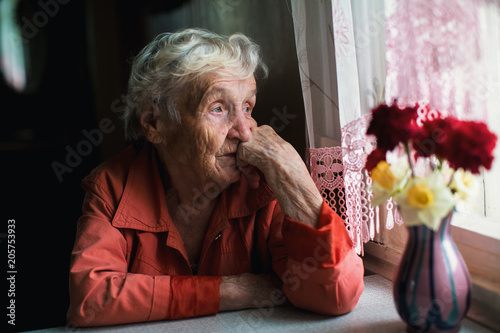 Elderly woman looks sadly out the window. photo