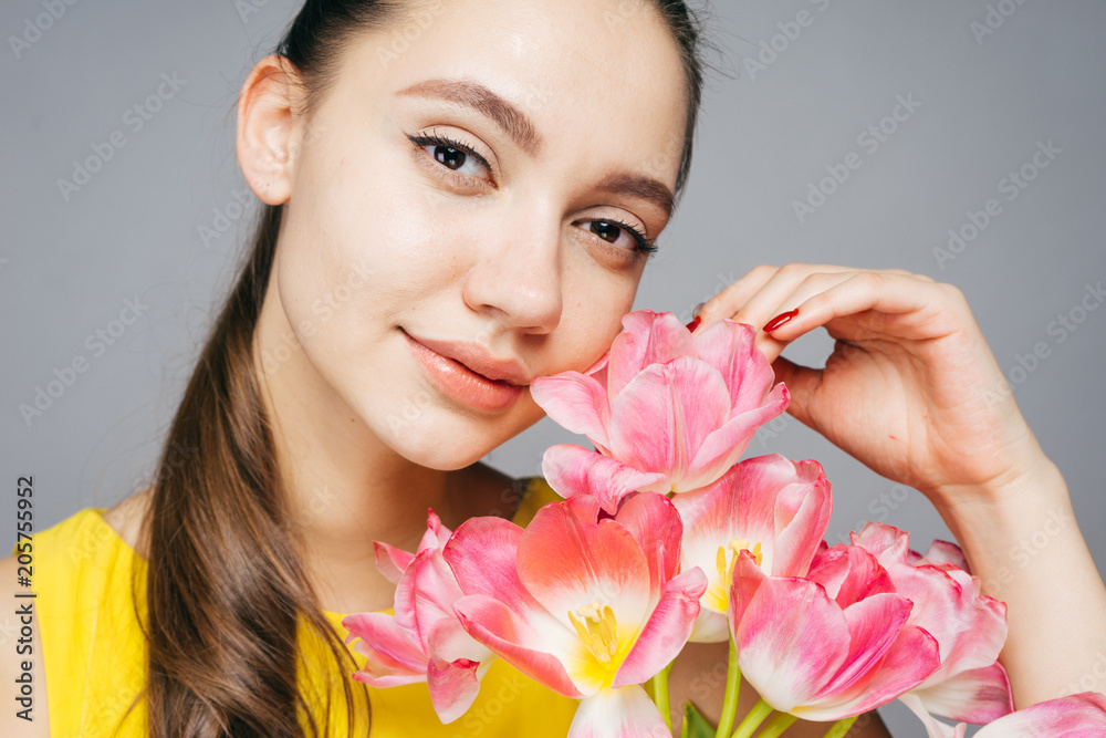 beautiful attractive woman in a yellow dress holds in her hands fragrant pink flowers and looks at the camera beautiful attractive woman in a yellow dress holds in her hands fragrant pink flowers and looks at the camera